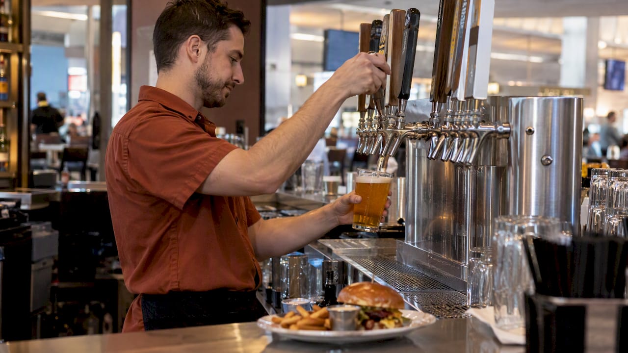 Bartender pouring beer beside airport pub fare